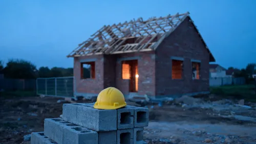 Rodinný dom v štádiu hrubej stavby s lešením a stavebnými materiálmi na pozemku