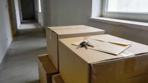Sťahovacie krabice pred bytovým domom a mladý muž s dokumentmi v ruke