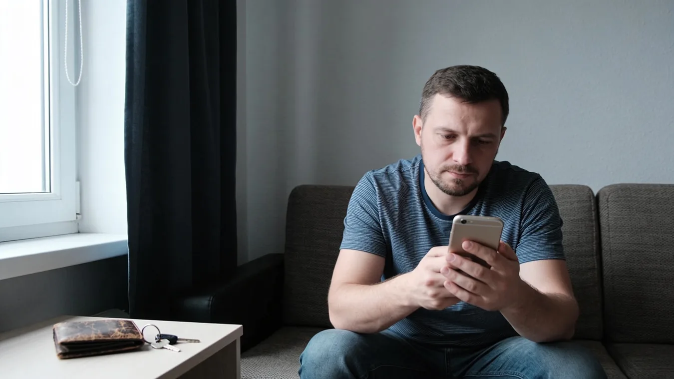 Muž doma pokojne kontroluje mobil po vybavení úveru
